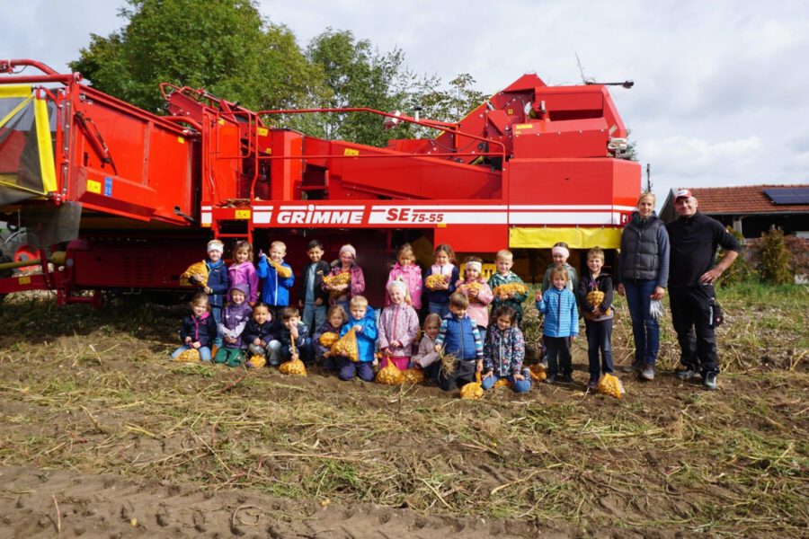 Kinder stehen auf einem Acker vor dem Kartoffelernter
